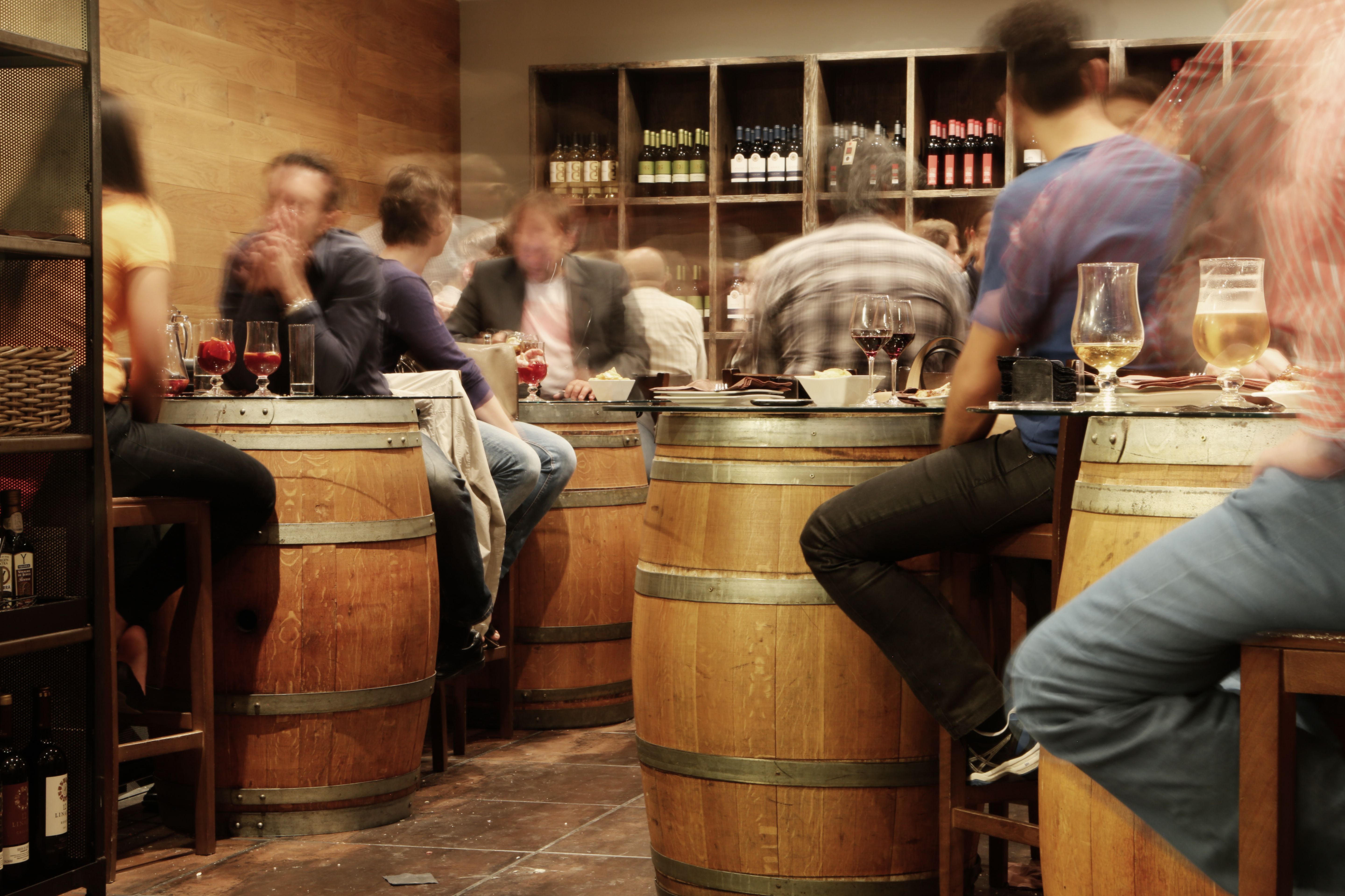 A lively bar with people sitting and chatting around wine barrel tables